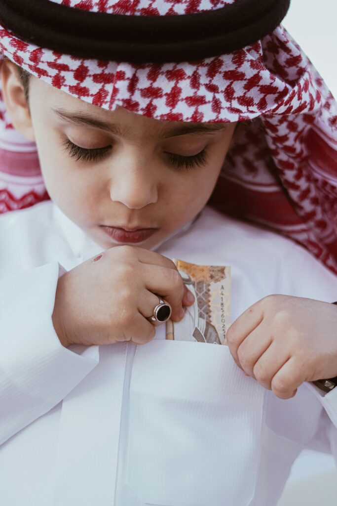 Portrait of a Cute Boy in a Traditional Headscarf and Wear Putting a Banknote in a Pocket of his Shirt